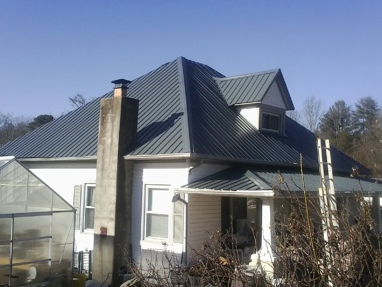 Dark blue standing seam metal roof on a white farmhouse with dormer — Slate & Tile Roof Repair by Roofing Brothers in Minden City