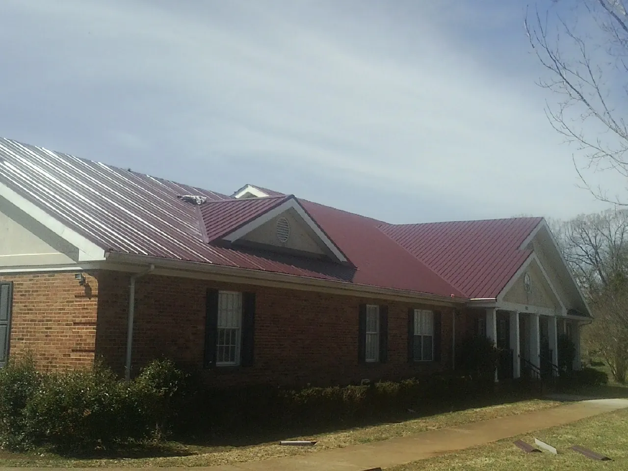 Red metal roof with gabled entries on a long brick building, from a Hail Damage Roof Repair job in Minden City
