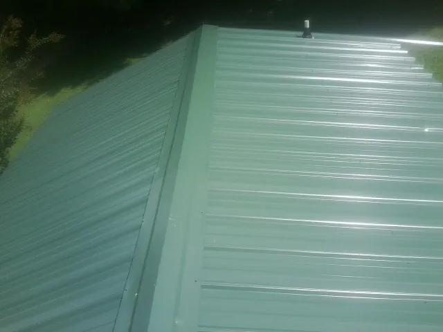 New green metal panels meeting at the ridge of a roof — Flat Roof Repair work by our crew in Minden City