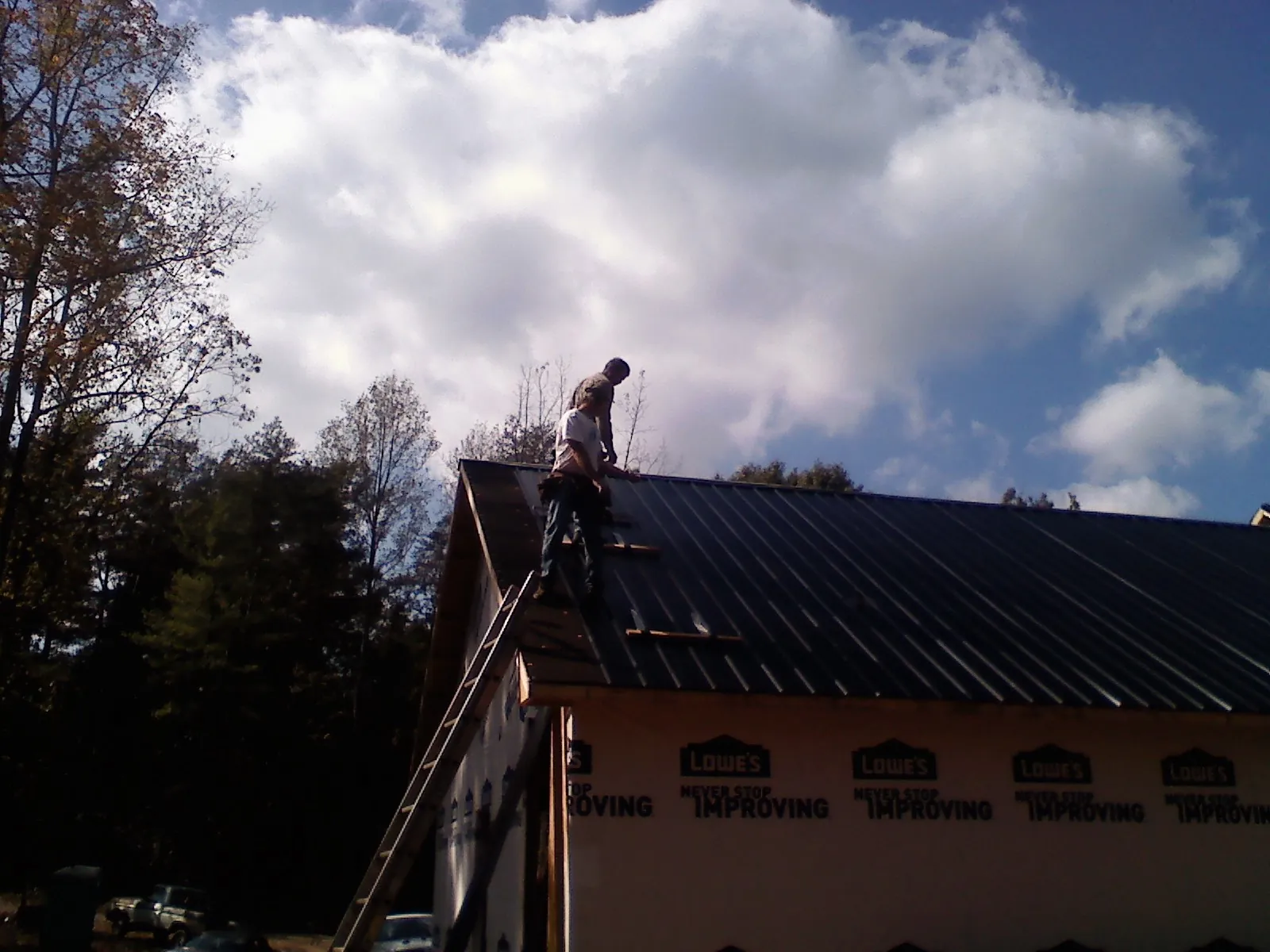 Roofer fastening dark metal panels high against a cloudy sky, from a Roof Inspection job in Minden City
