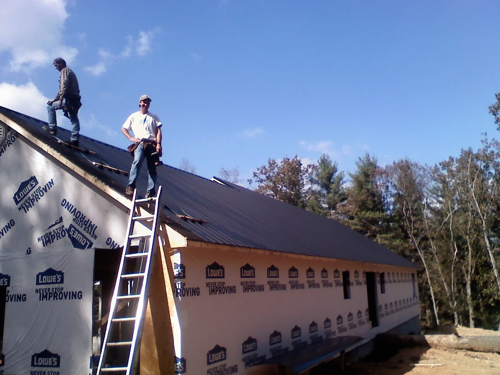 Two roofers standing on a long dark metal roof over a wrapped building in Minden City