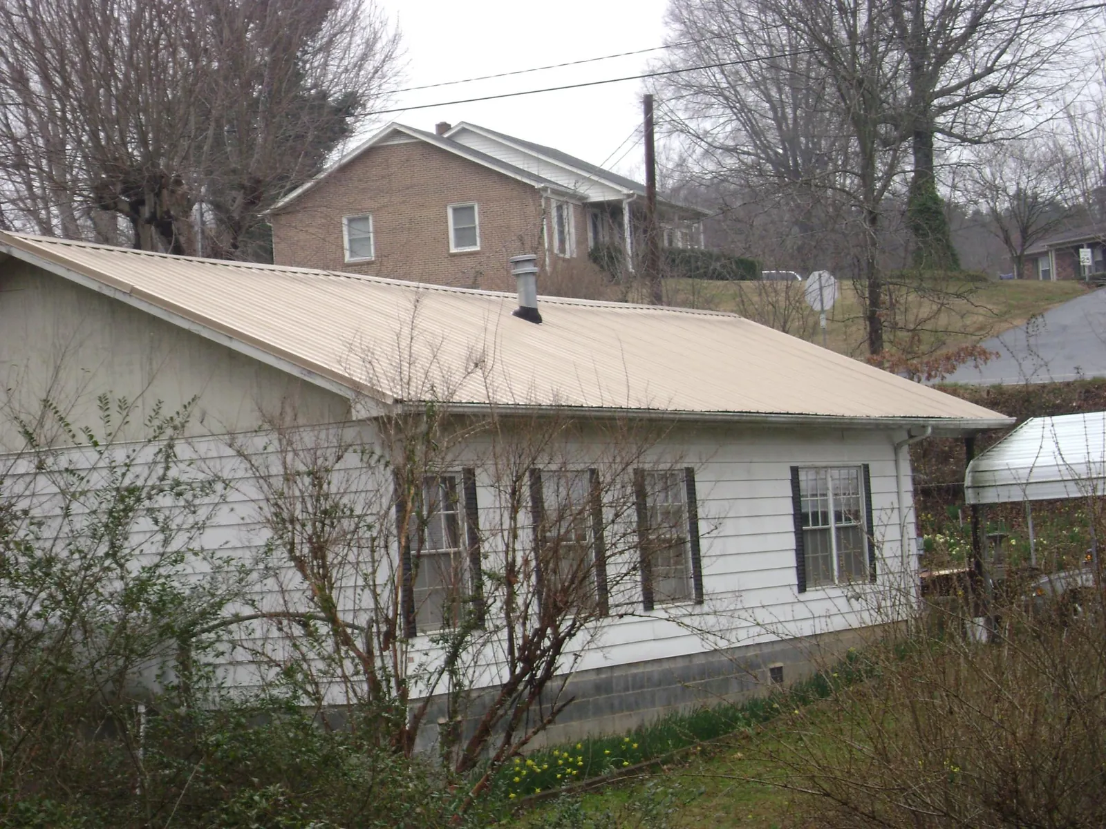 Tan metal roof on a white sided house set into a hillside — Commercial Roofing by Roofing Brothers in Minden City